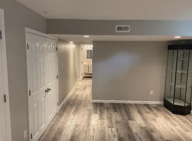 A finished basement hall with gray walls, white six-panel doors and a wood-look vinyl floor