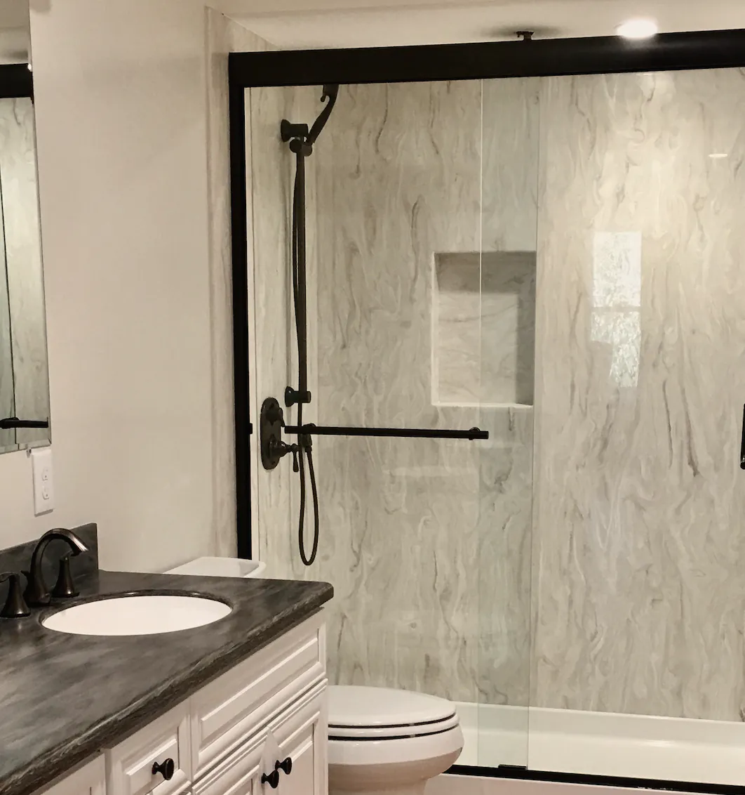 A shower with marble-look walls, a built-in niche, sliding glass doors and a bronze handheld shower