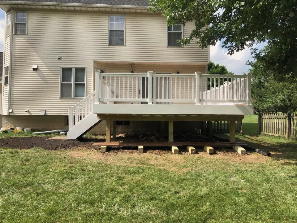 A raised composite deck with white vinyl railings and stairs at the back of a sided colonial