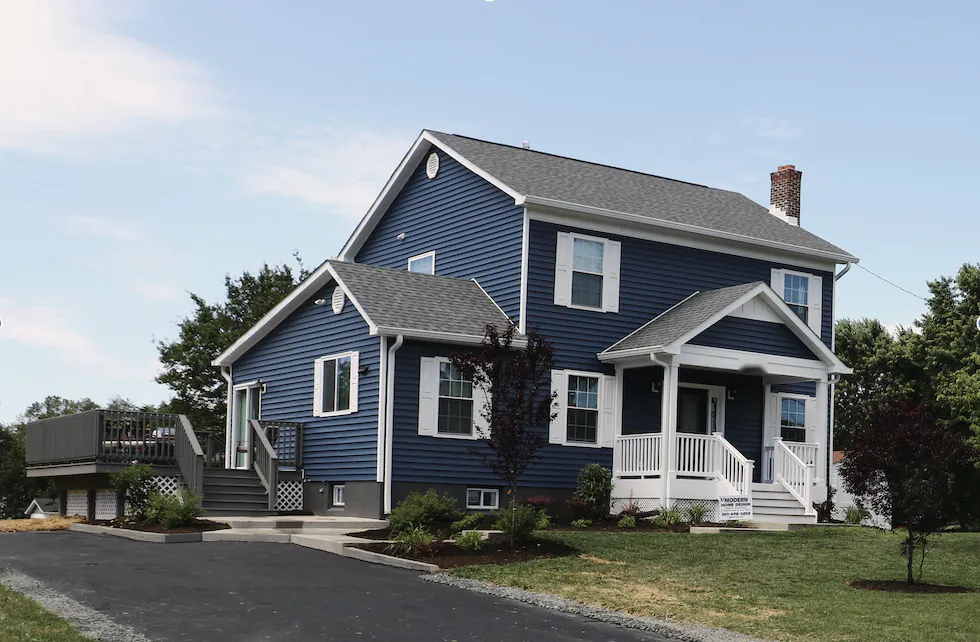 A new two-story house in navy siding with a front porch, and the Modern Home Design sign in the yard