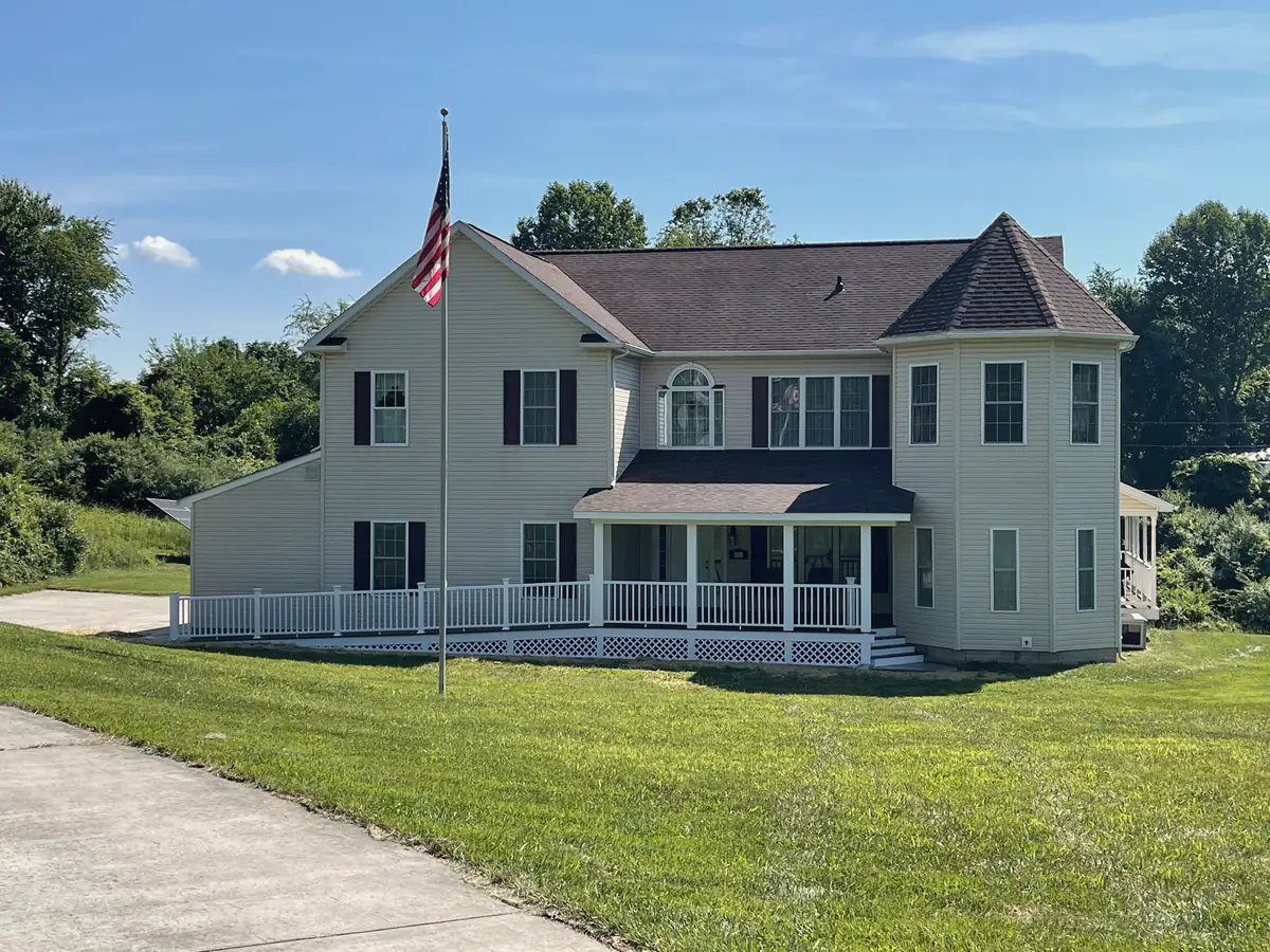 A large two-story house with a corner turret and a wraparound front porch with white railings