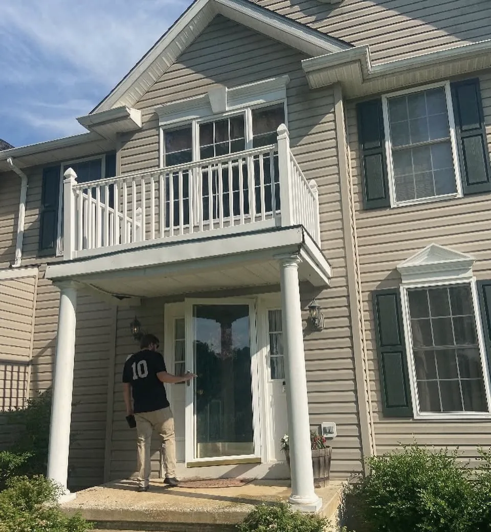 A front entry before the work: a balcony on two columns over the door of a sided colonial