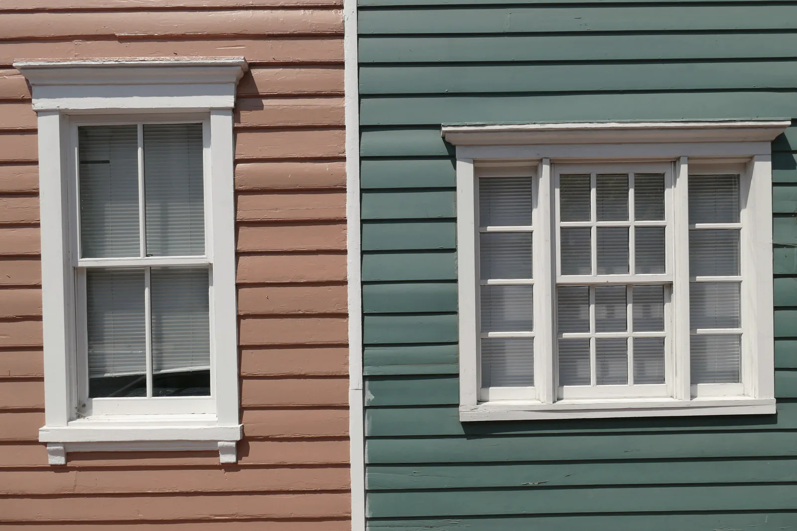 Two houses side by side in painted lap siding, each with a white-trimmed double-hung window